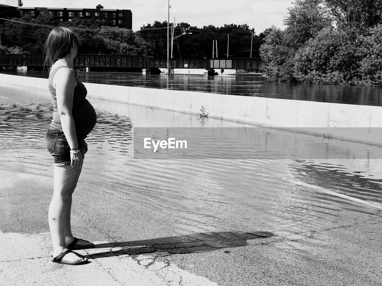 Side view of pregnant woman standing by lake on sunny day