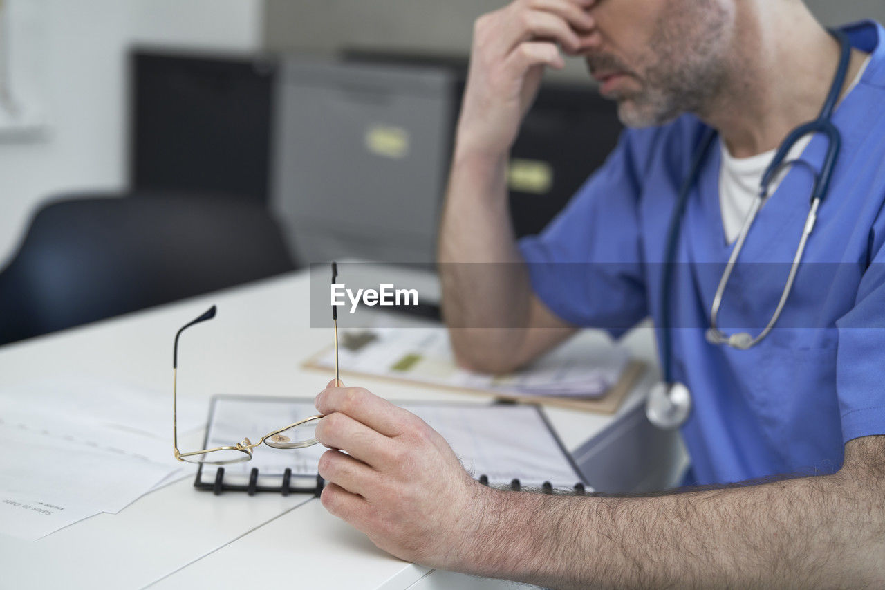 Tired mature doctor sitting at desk in clinic