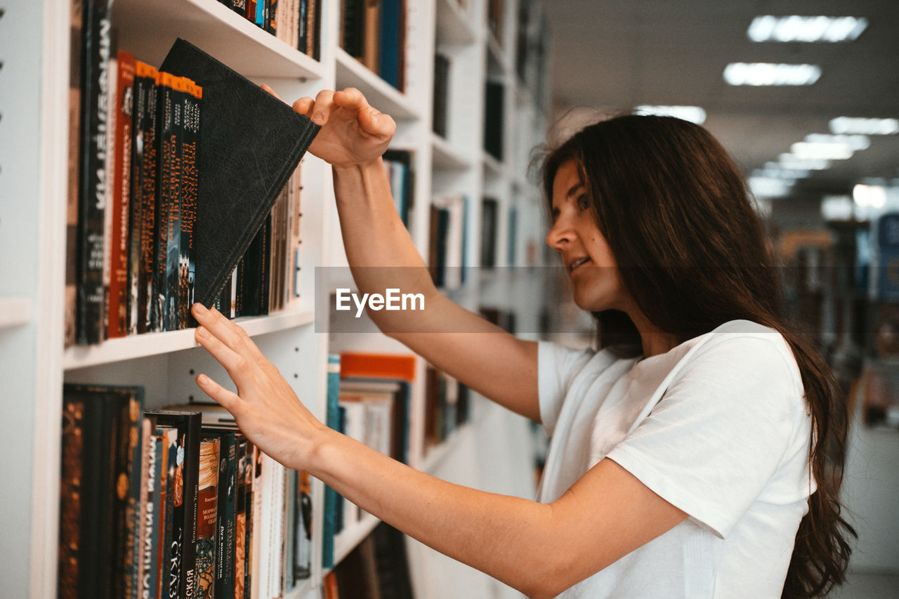 WOMAN HOLDING BOOK WHILE STANDING IN SHELF