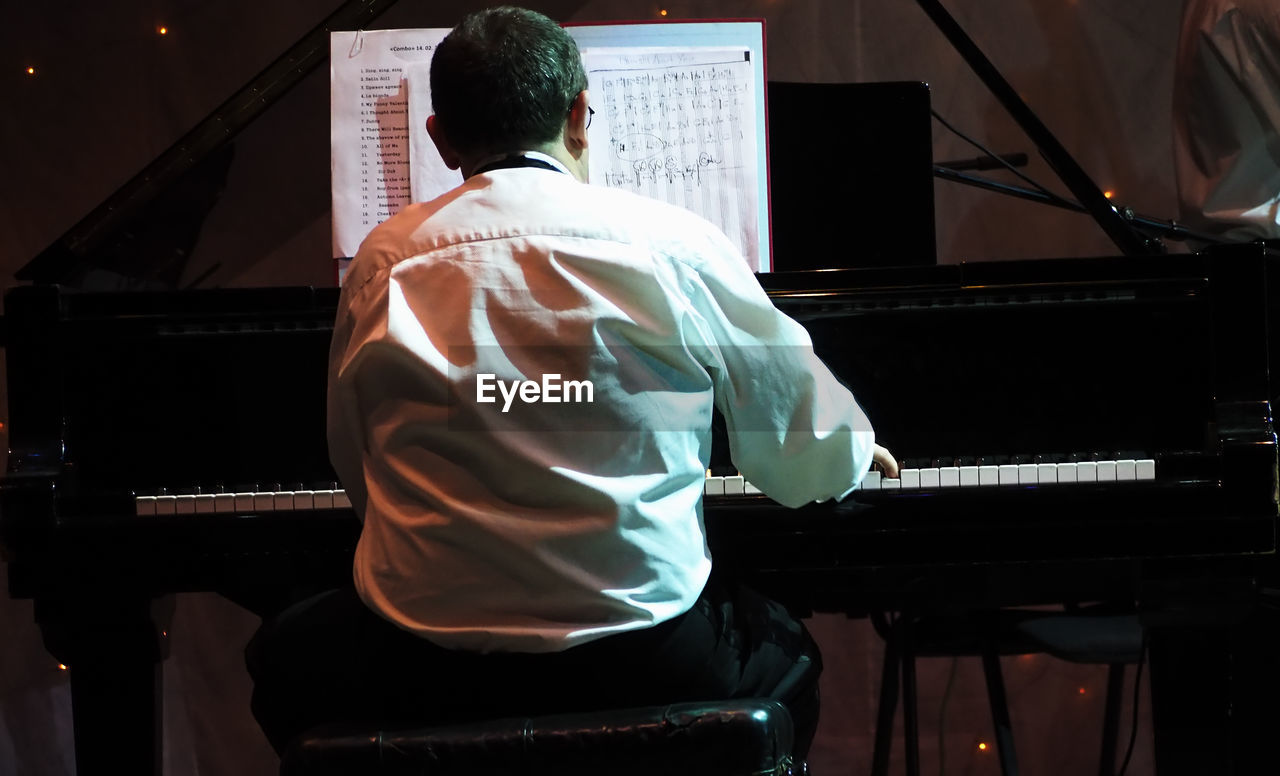 REAR VIEW OF MAN PLAYING PIANO AT NIGHTCLUB