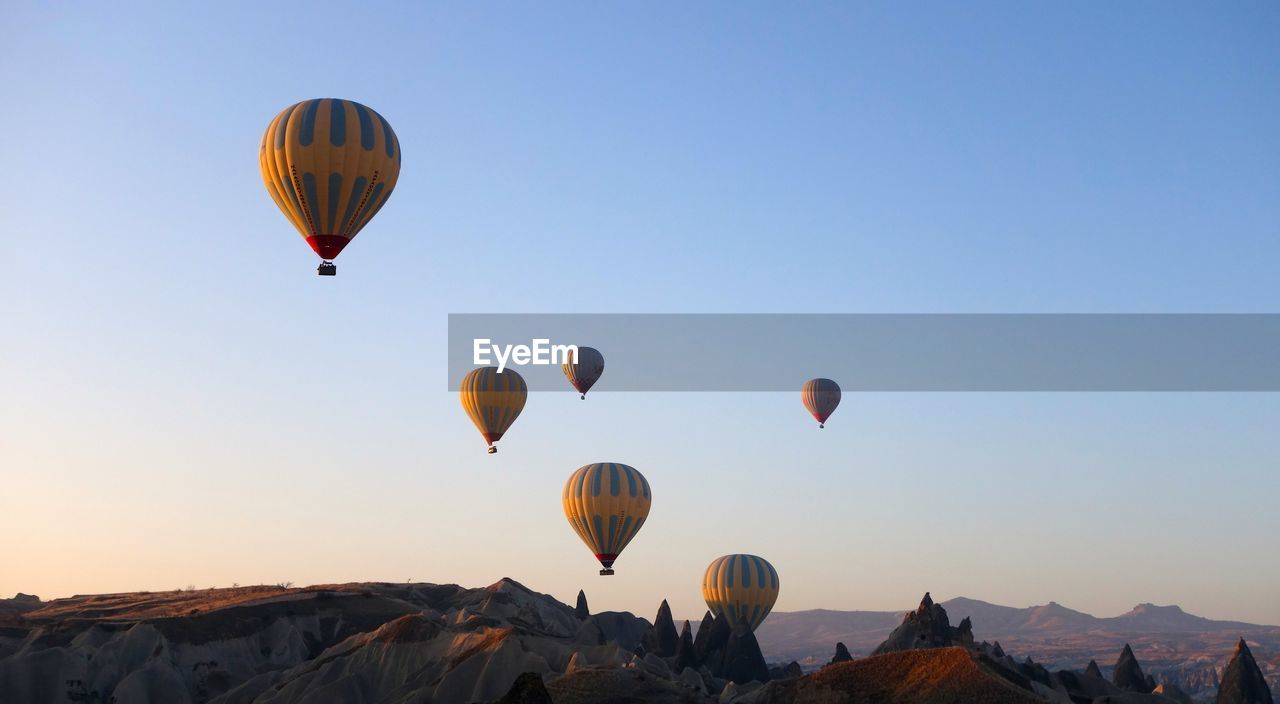 HOT AIR BALLOONS FLYING OVER ROCKS AGAINST CLEAR BLUE SKY