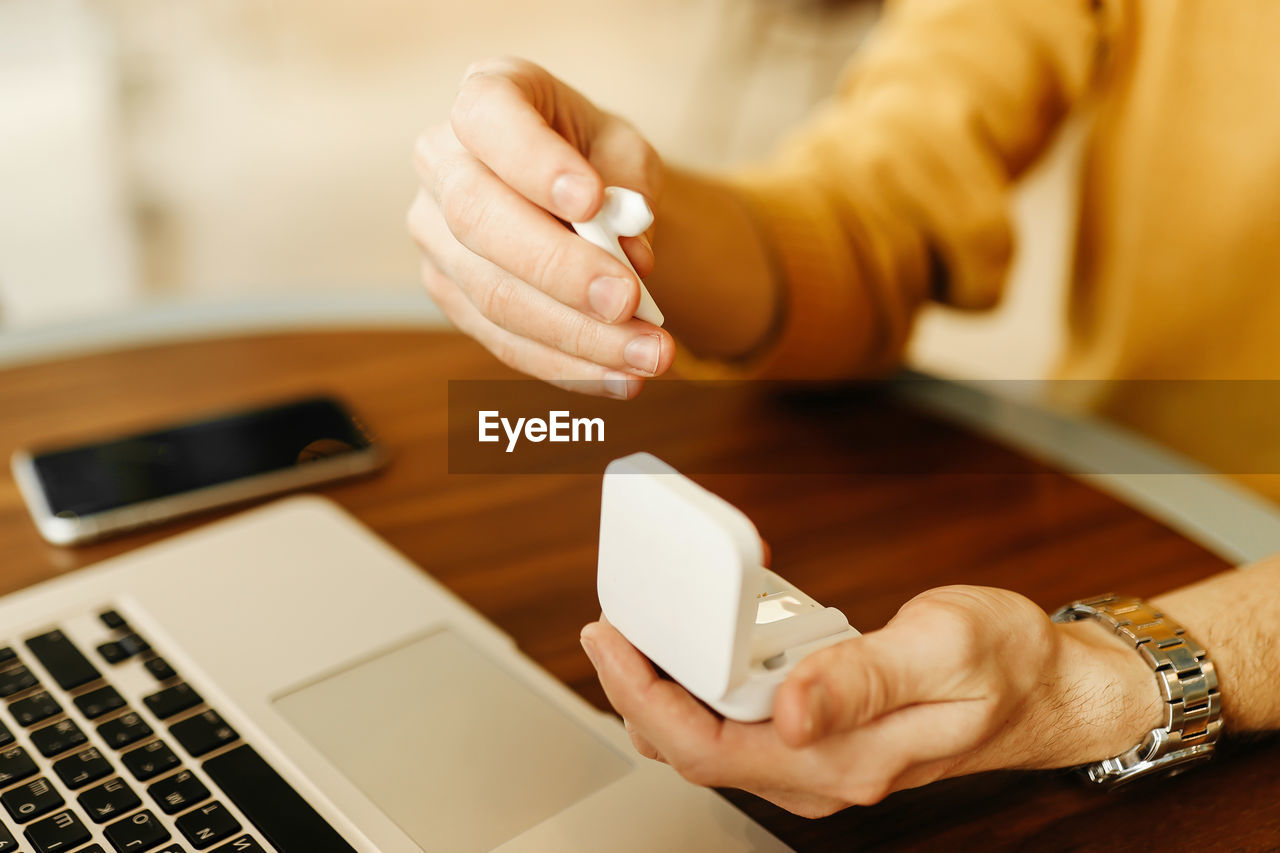 Close up of human hands holding wireless technology headphones phone laptop on the table