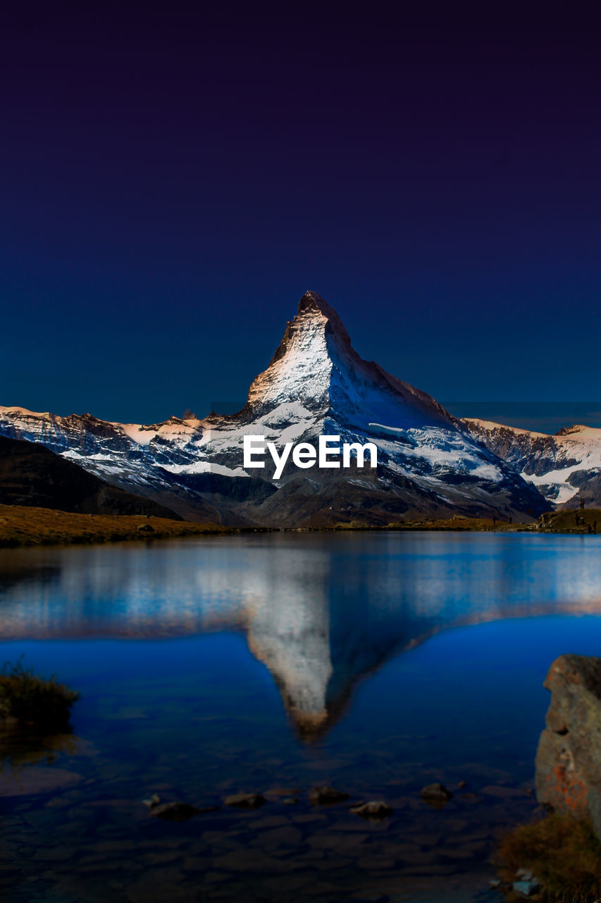 Scenic view of lake and snowcapped mountains against clear blue sky