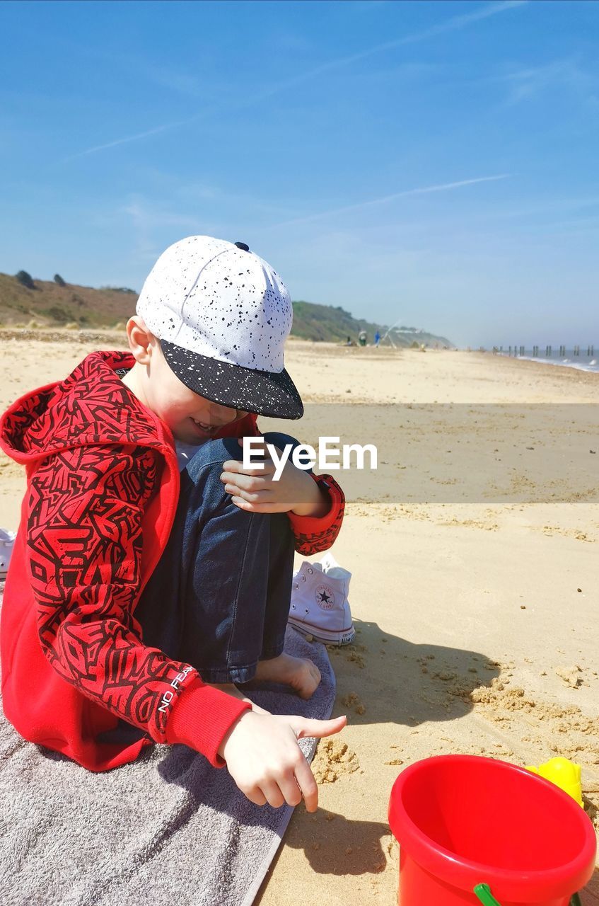 Full length of boy sitting on beach against sky