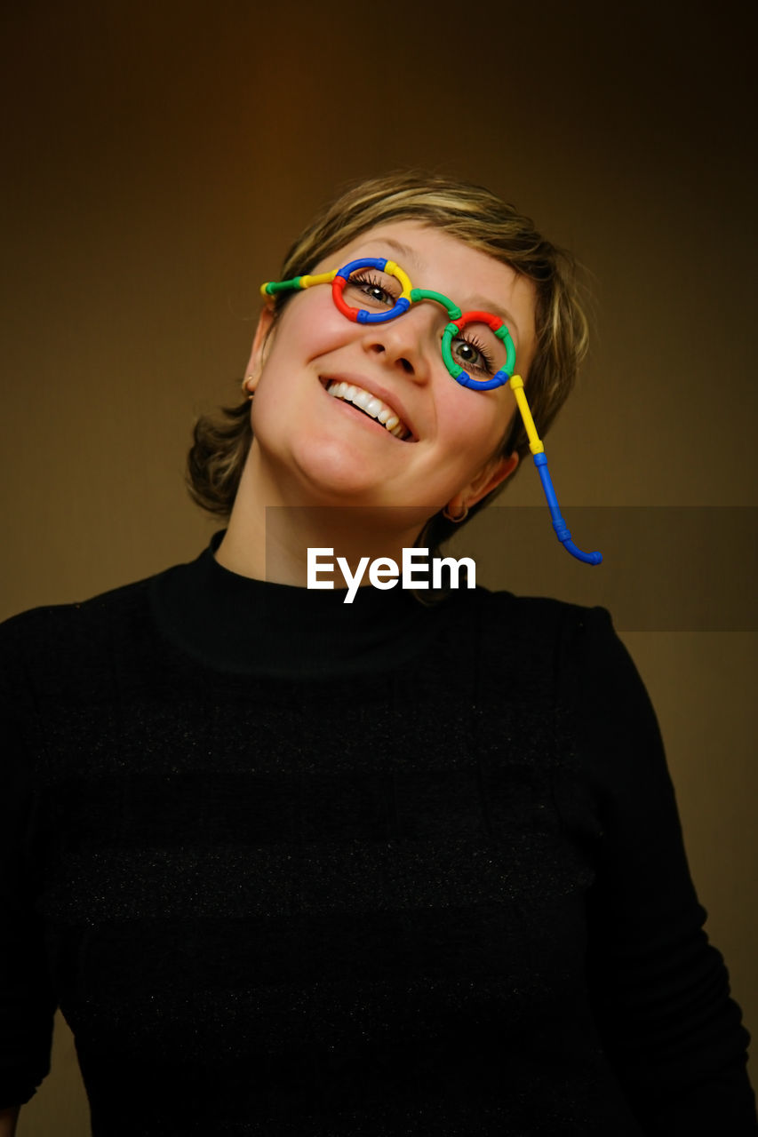 Portrait of smiling woman wearing novelty glasses against colored background