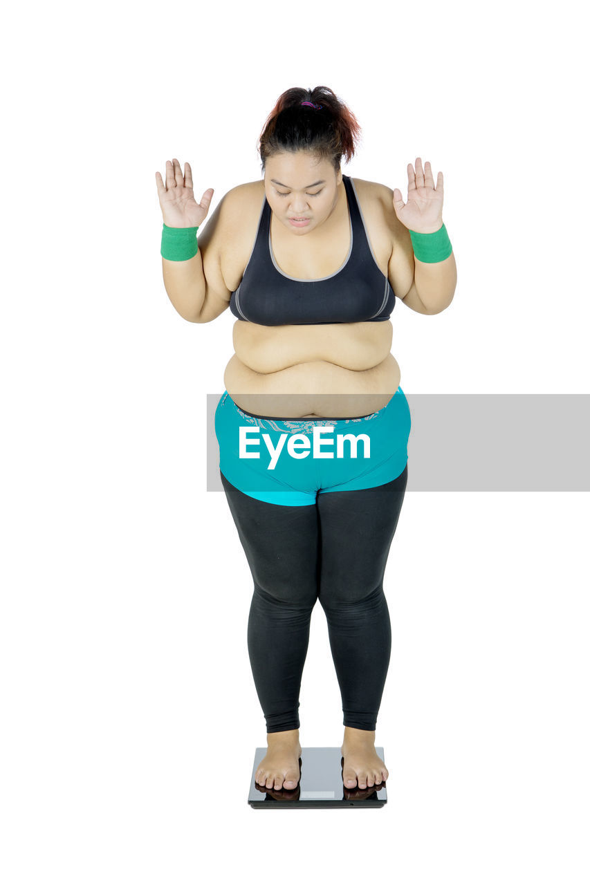 Full length of woman standing on weight scale against white background