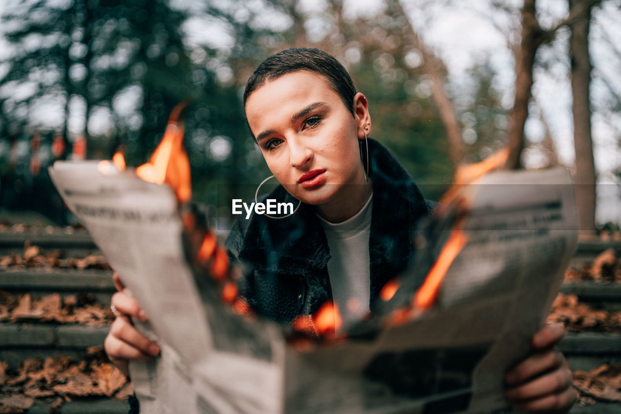Portrait of beautiful young woman holding camera at tree