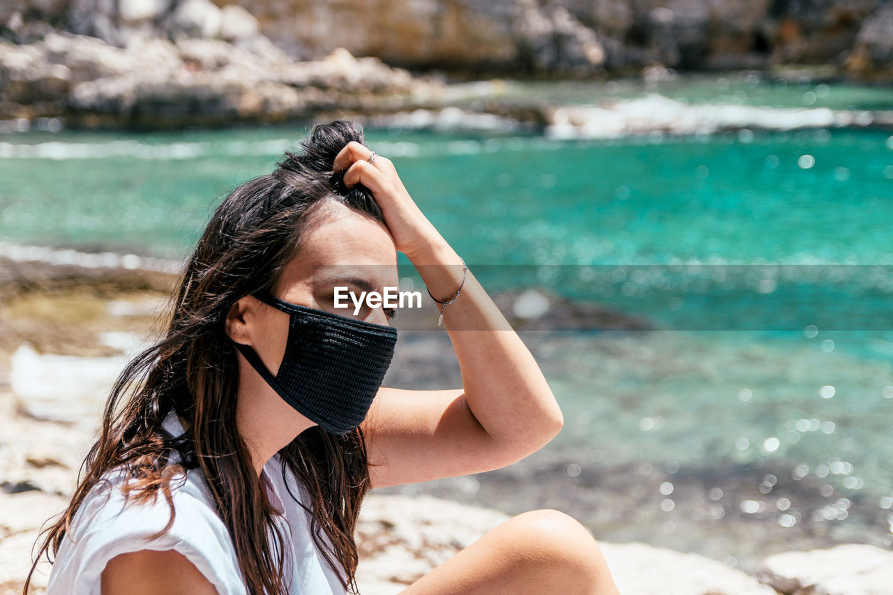 Portrait of a young woman wearing black protective mask on beach in summer. tourist, corona, covid.
