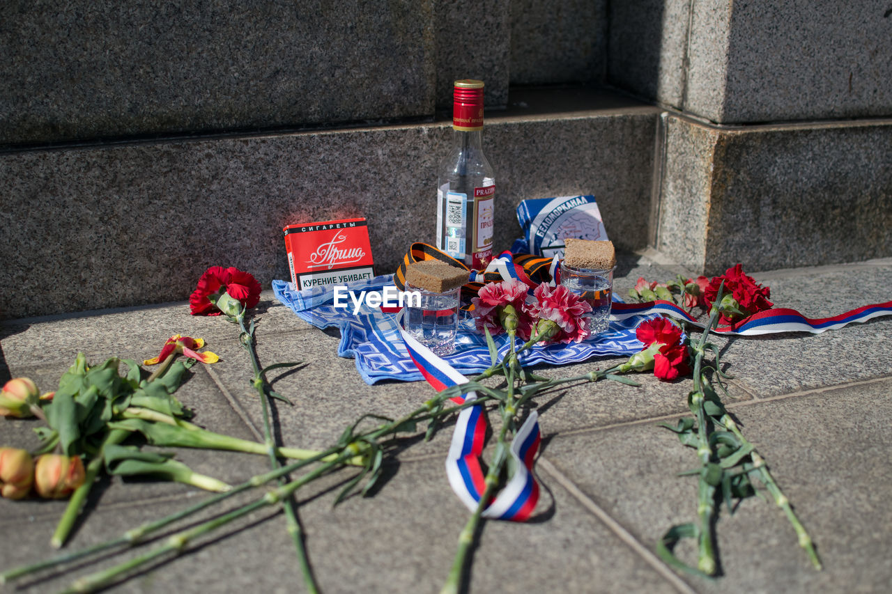 HIGH ANGLE VIEW OF VARIOUS FLOWERS IN BOTTLE ON SIDEWALK