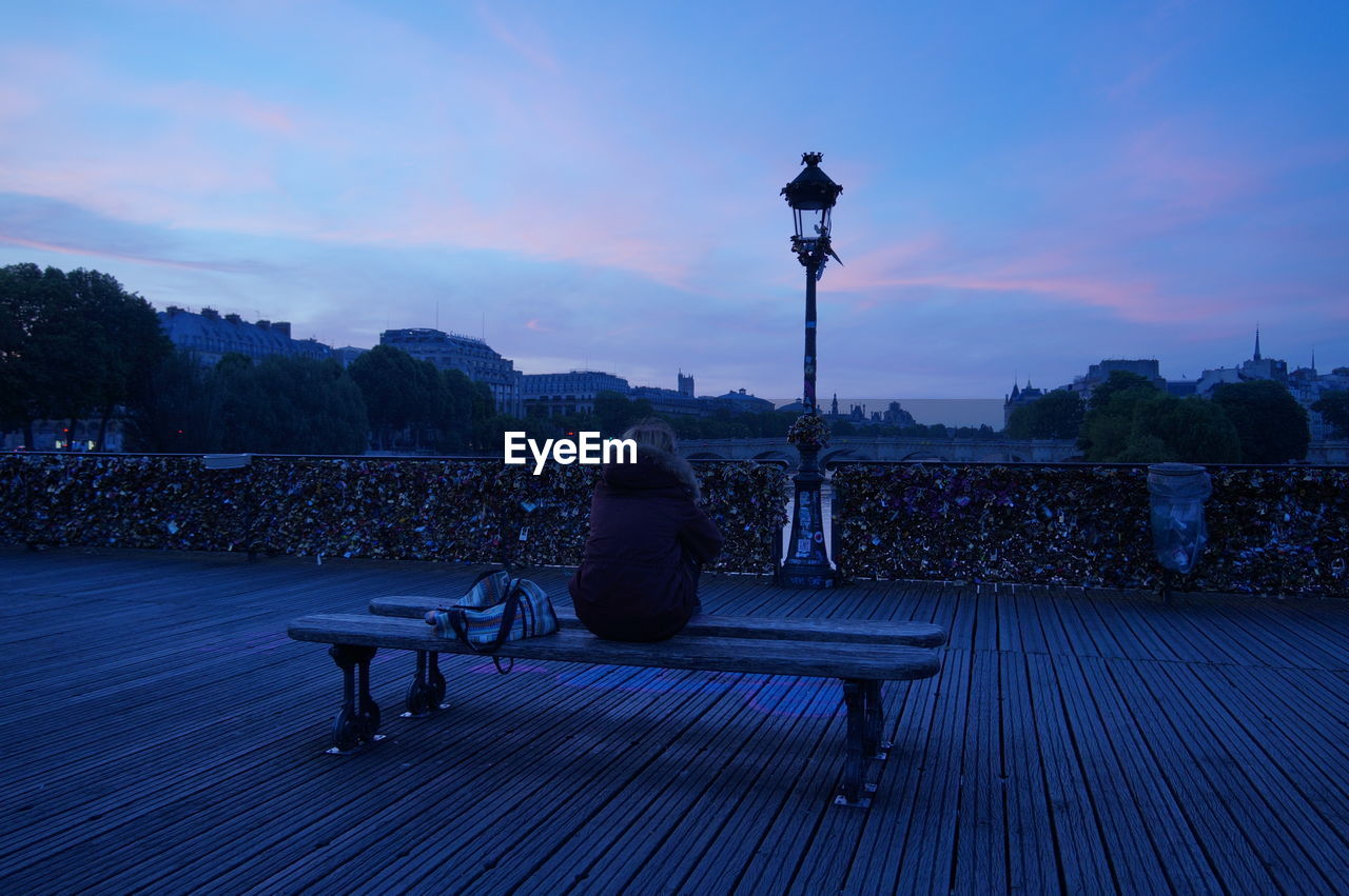 Rear view of woman sitting on bench over pont des arts at dusk
