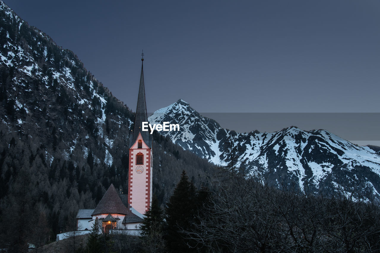 Church by snowcapped mountains against clear sky during winter