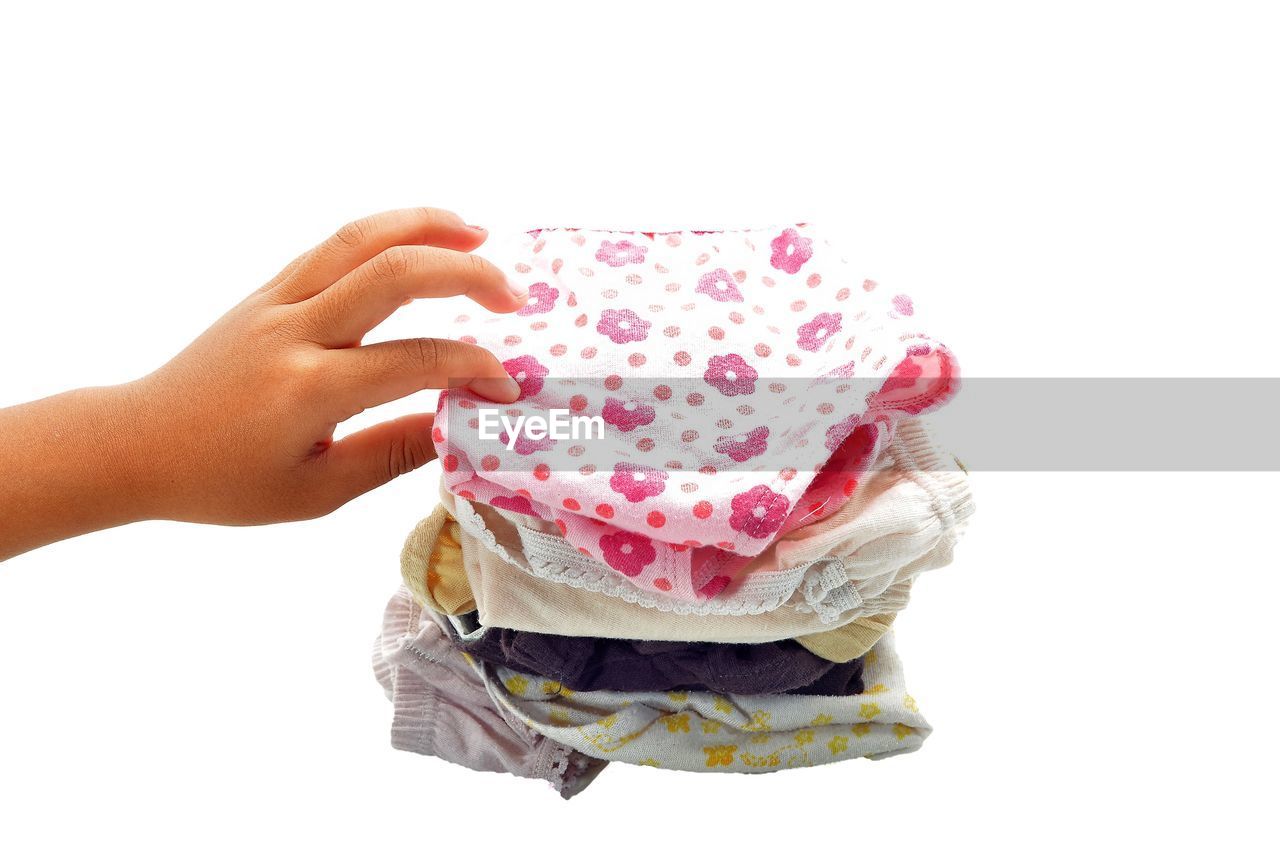 Close-up of hand holding kids garment  against white background