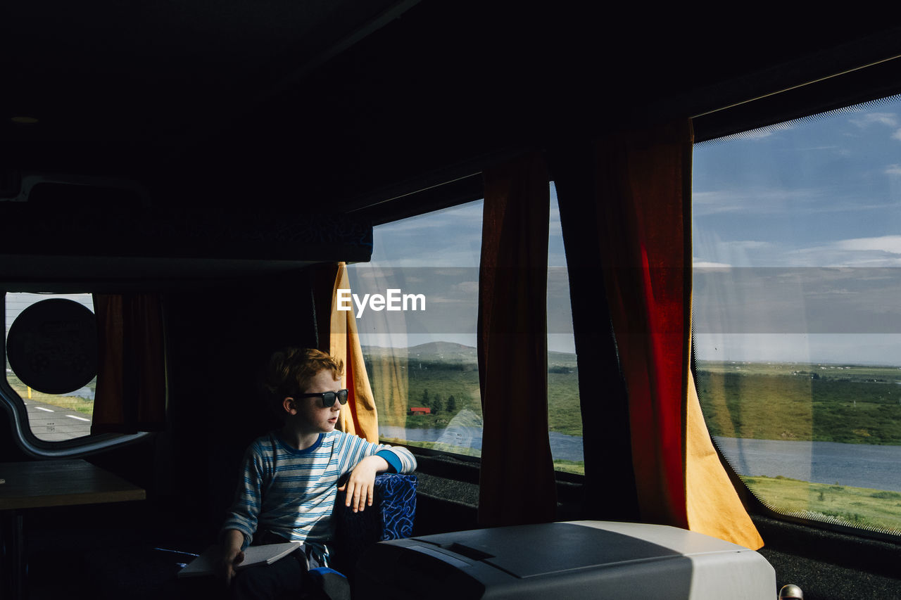 Boy wearing sunglasses looking through window while sitting in motor home