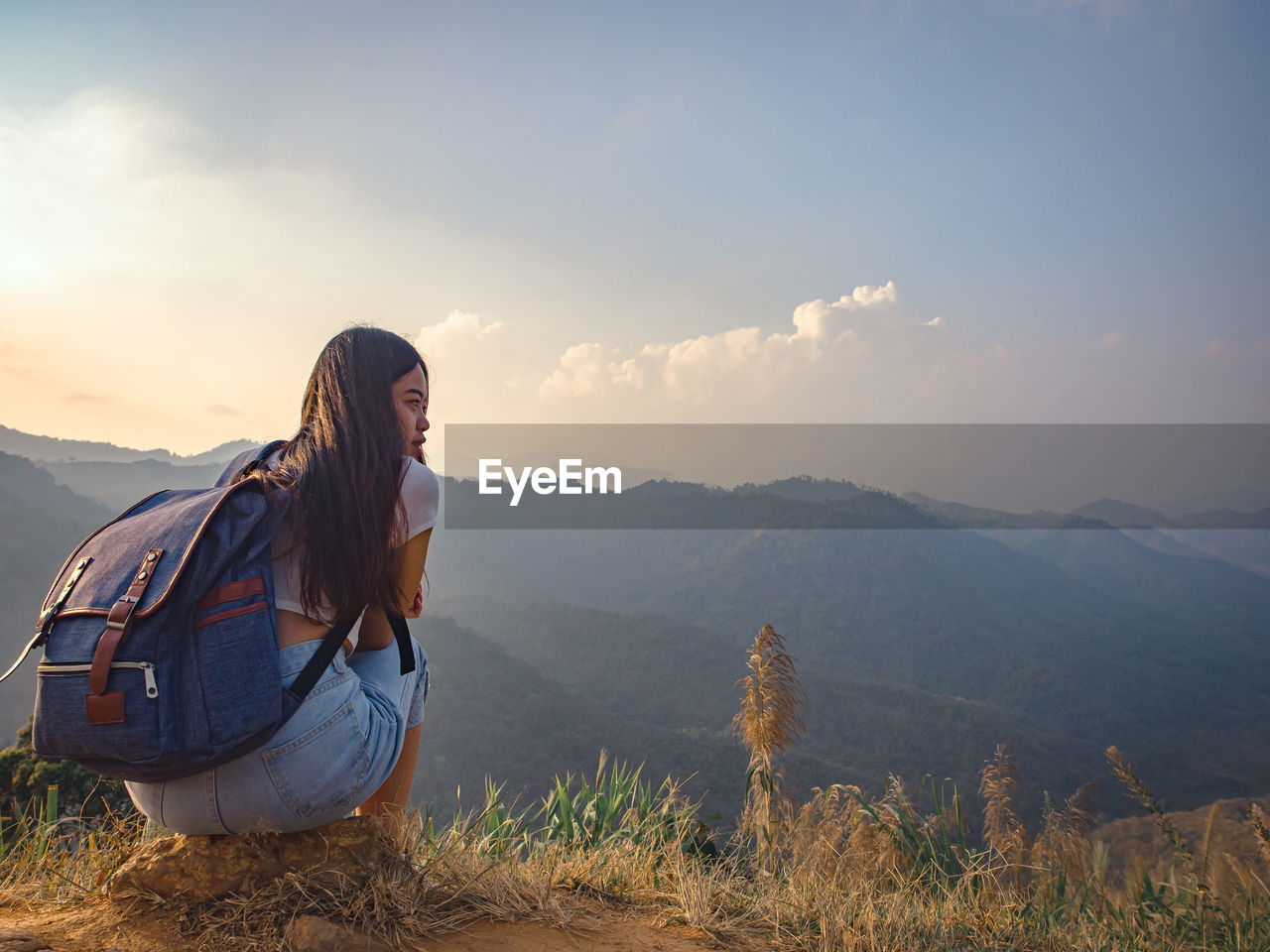 Backside of woman with backpack sitting to enjoy on mountains peak in the morning