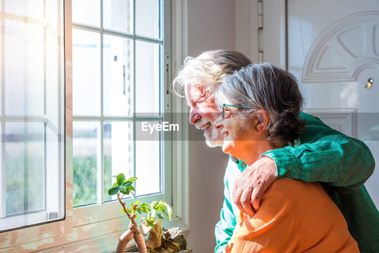 Couple looking through window while standing at home