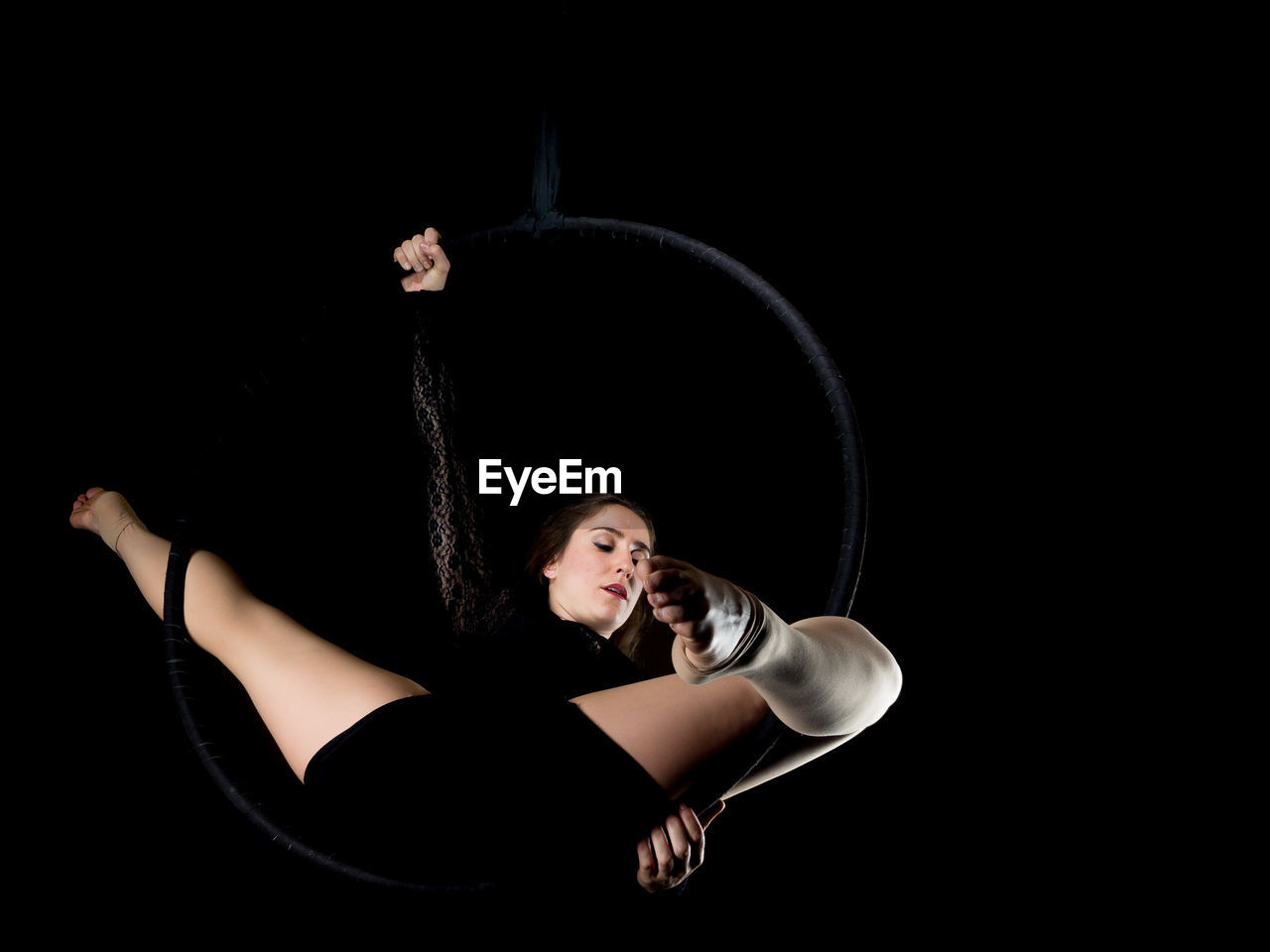 Low angle view of woman hanging on ring against black background