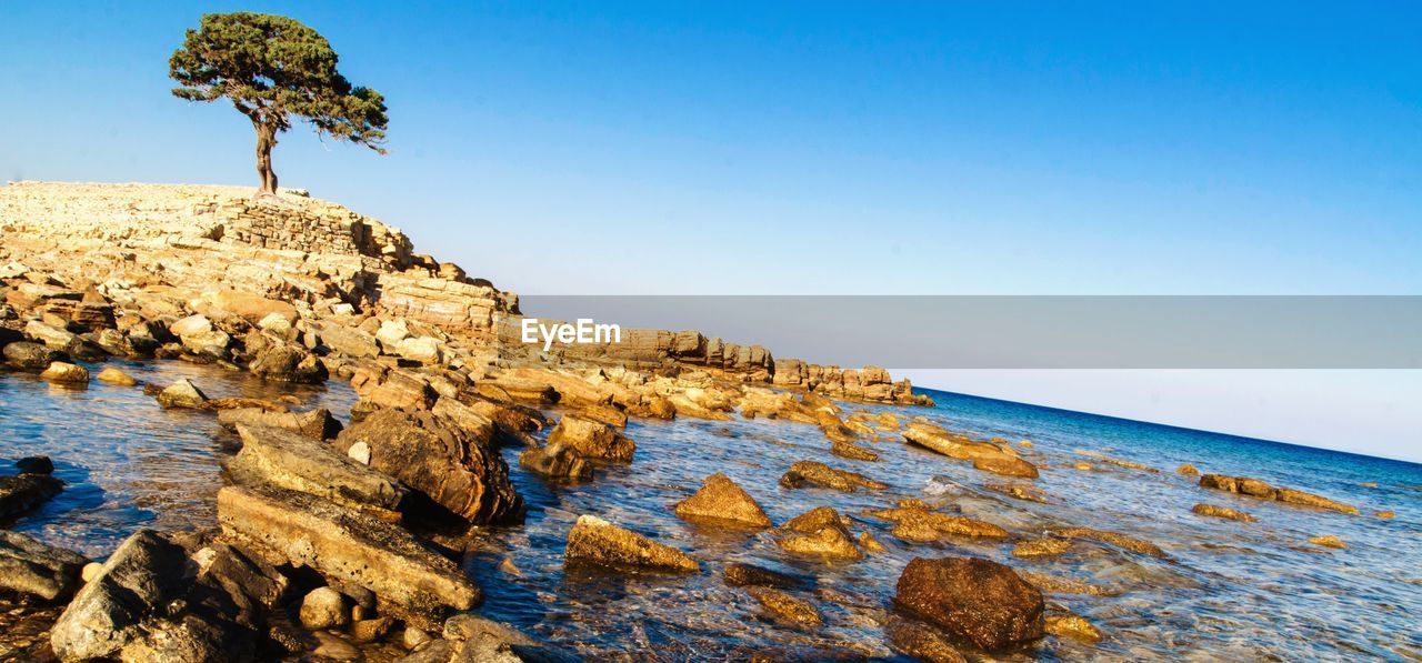 Rock formations by sea against clear blue sky