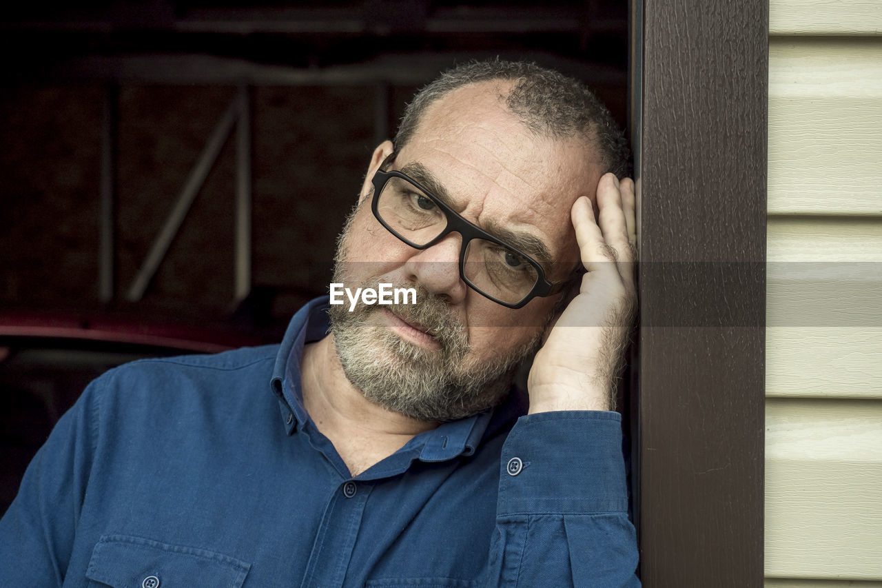 An adult pensive man in glasses leaned against a door jamb. outdoor portrait