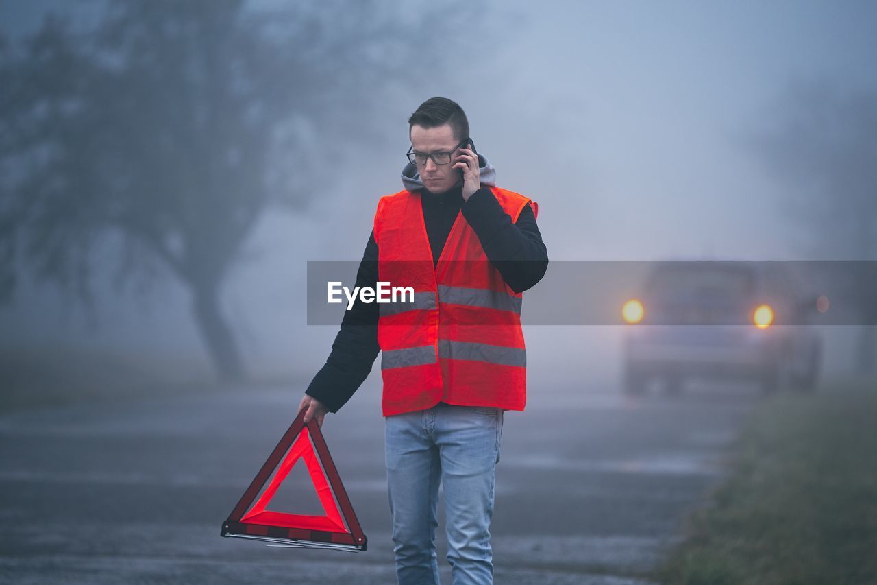 Man talking on phone while placing road sign during foggy weather