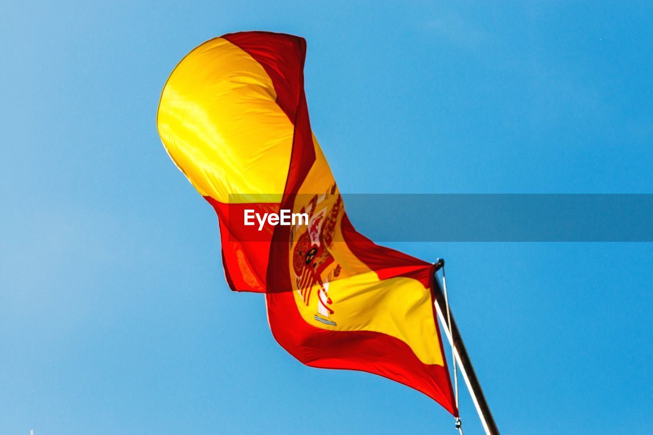 Low angle view of spanish flag fluttering against blue sky