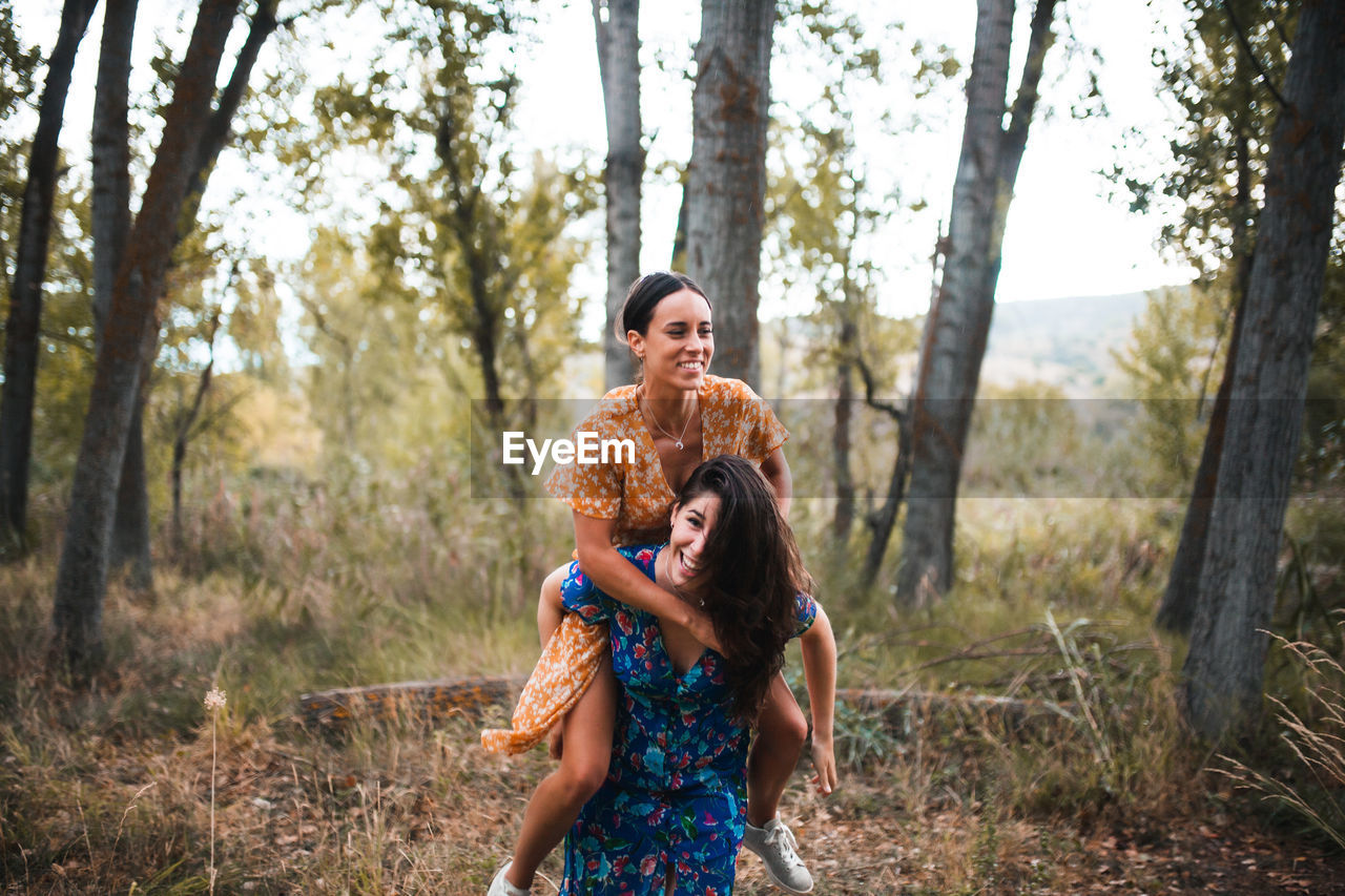 Woman piggybacking girlfriend in forest