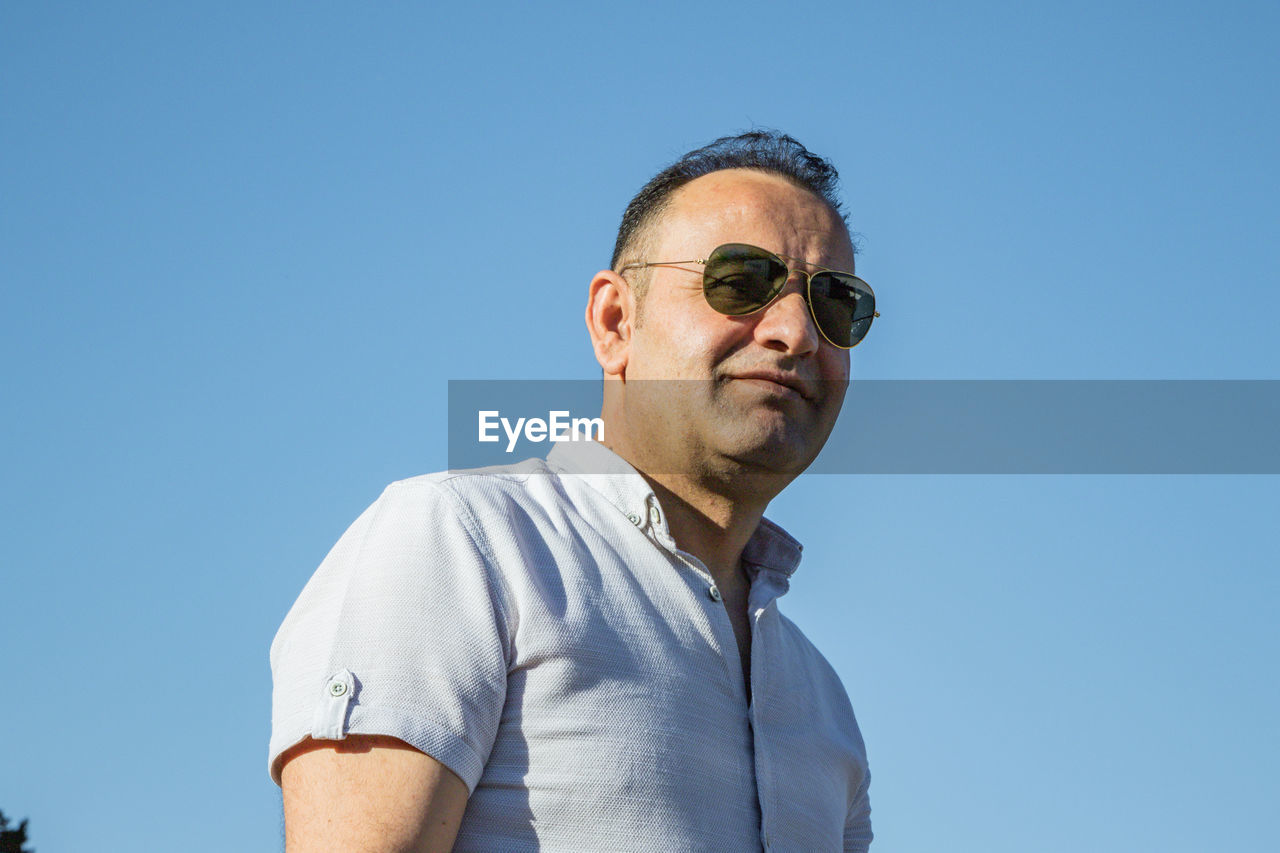 Low angle portrait of man against clear blue sky