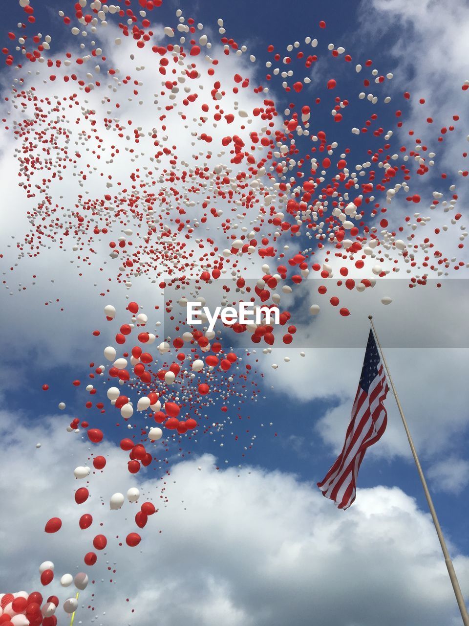 Low angle view of american flag with multi colored balloons in sky