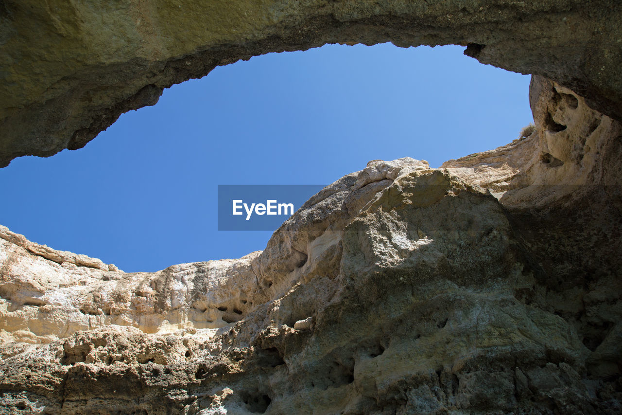 LOW ANGLE VIEW OF CLIFFS AGAINST CLEAR BLUE SKY