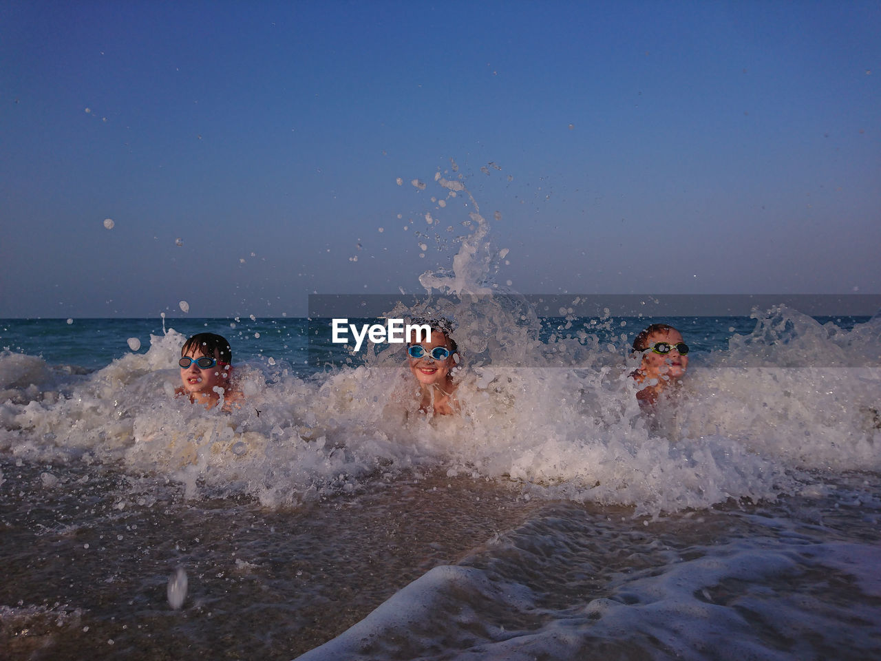 Boys swimming in sea against clear sky during sunset