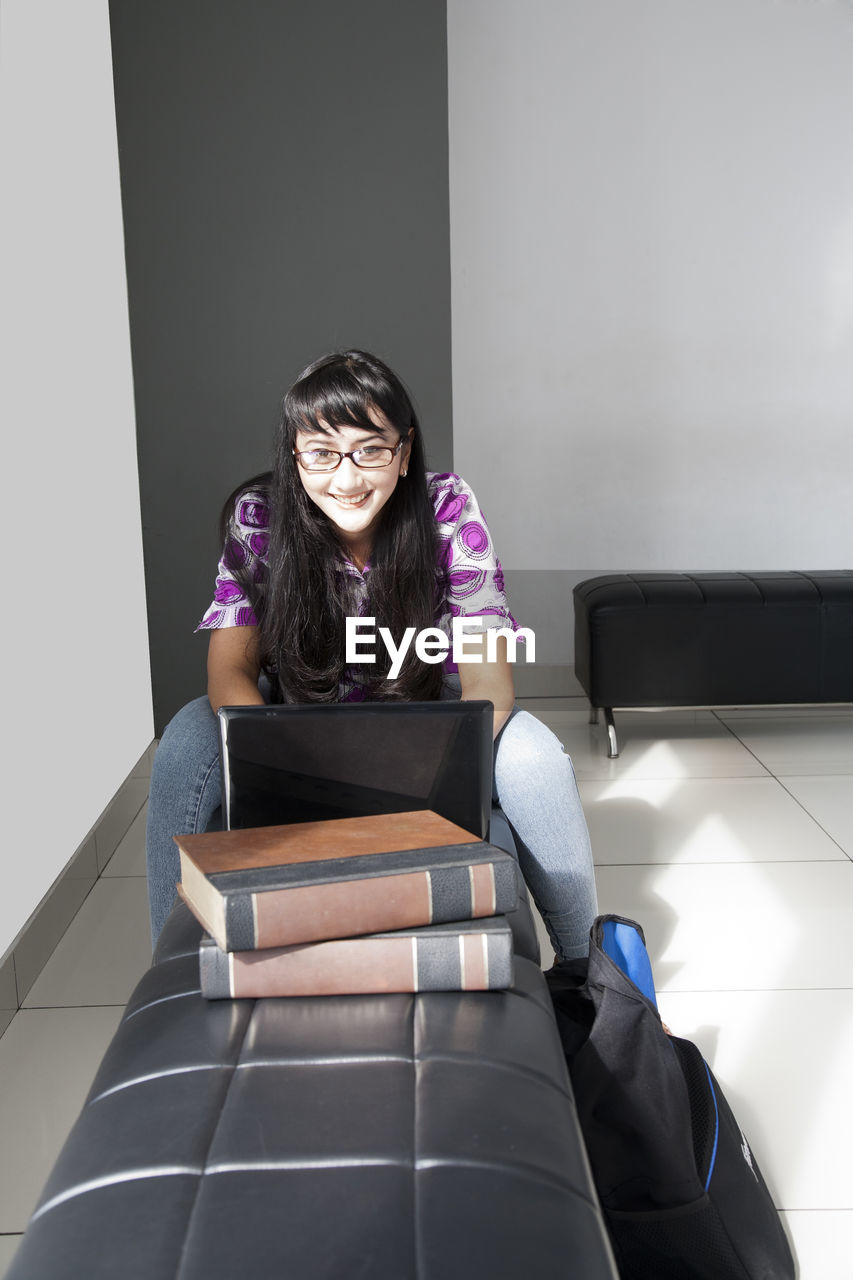 Portrait of woman using laptop while sitting on sofa at home