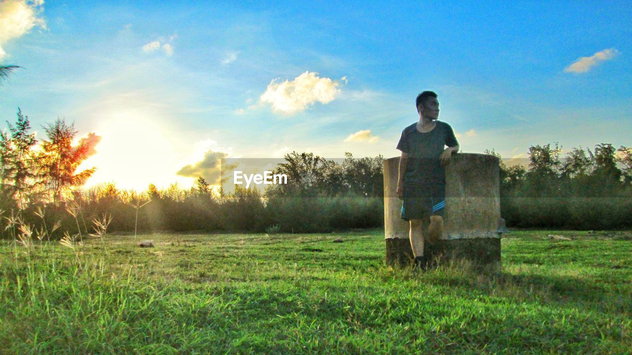 BOY STANDING ON FIELD AGAINST SKY