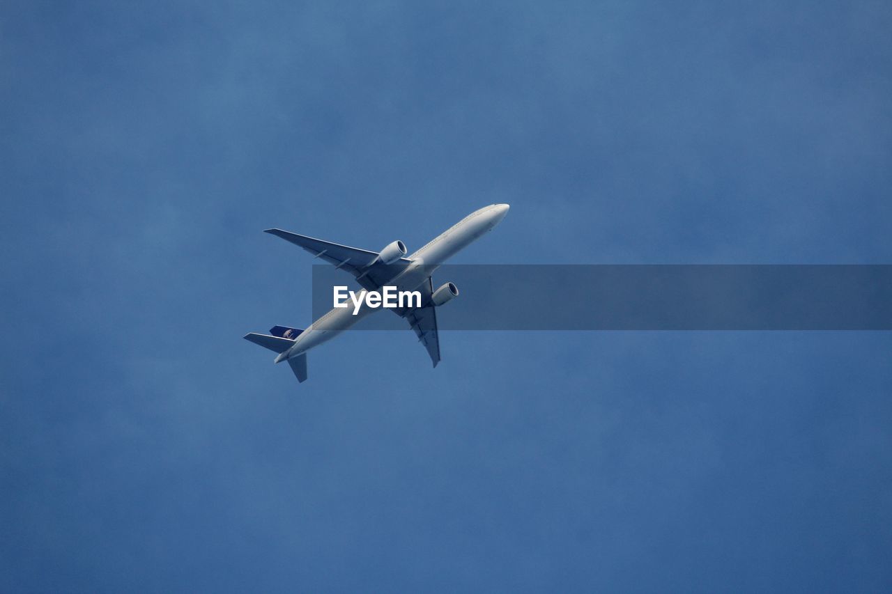 LOW ANGLE VIEW OF AIRPLANE IN FLIGHT AGAINST BLUE SKY