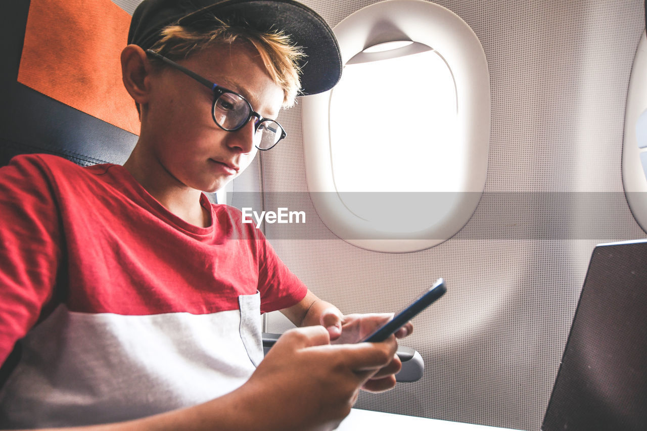 Cute boy using phone while sitting in airplane