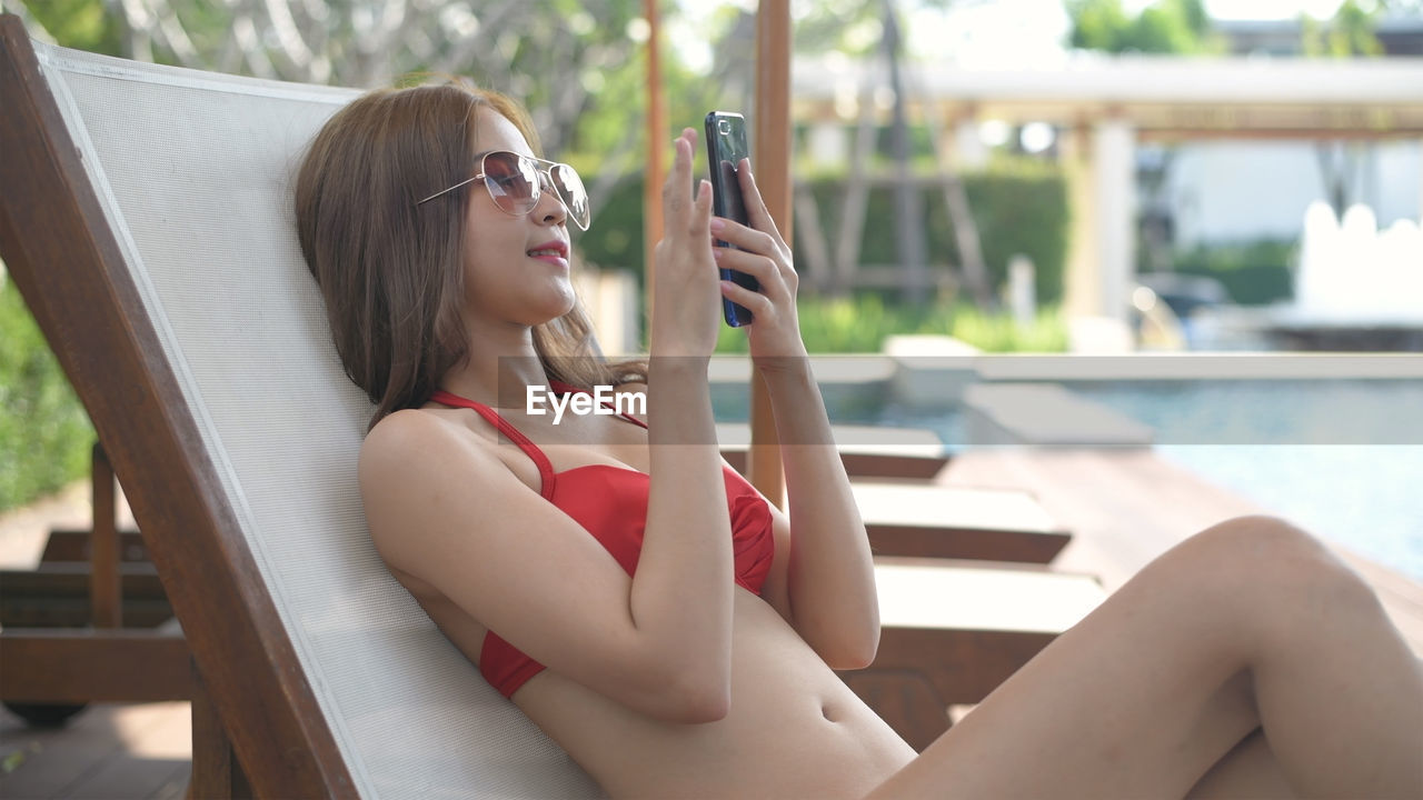 YOUNG WOMAN SITTING ON SWIMMING POOL AT RESORT