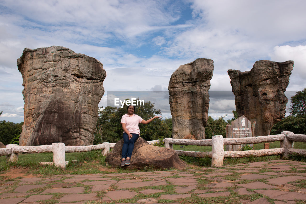 REAR VIEW OF MAN STANDING ON ROCKS AGAINST SKY