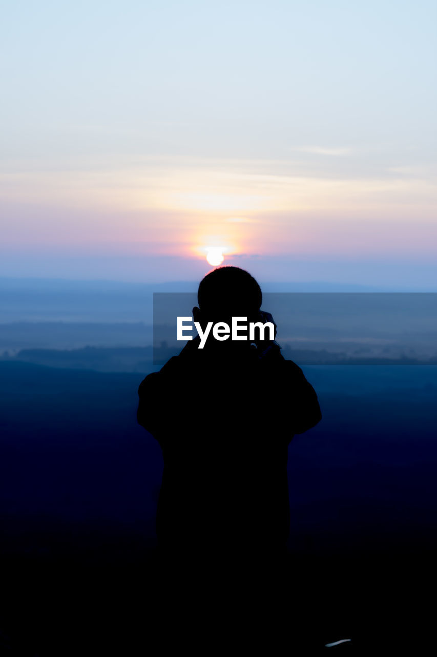 Silhouette man photographing while standing against sky during sunset