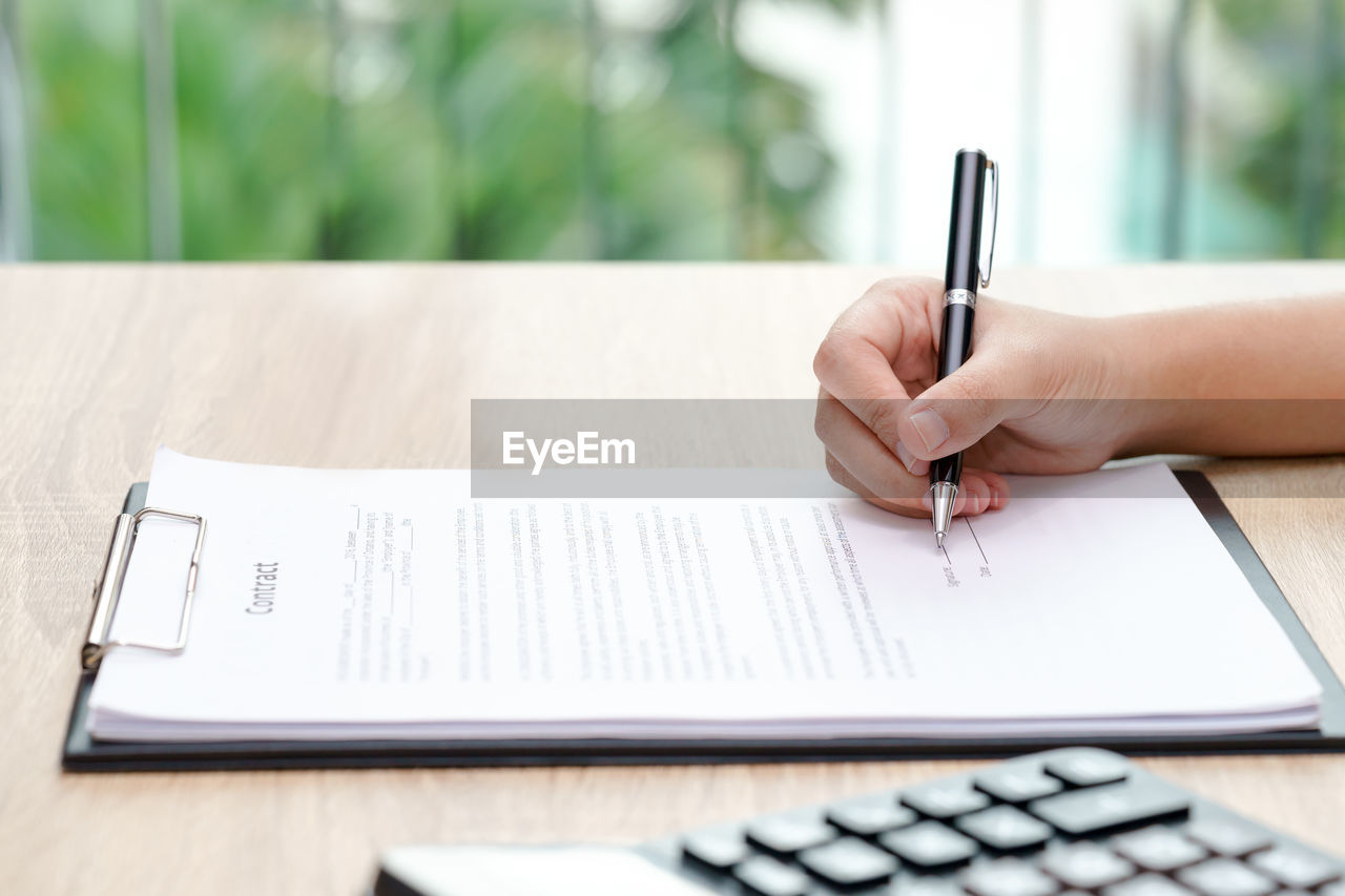 Cropped hand of businesswoman signing contract on table in office