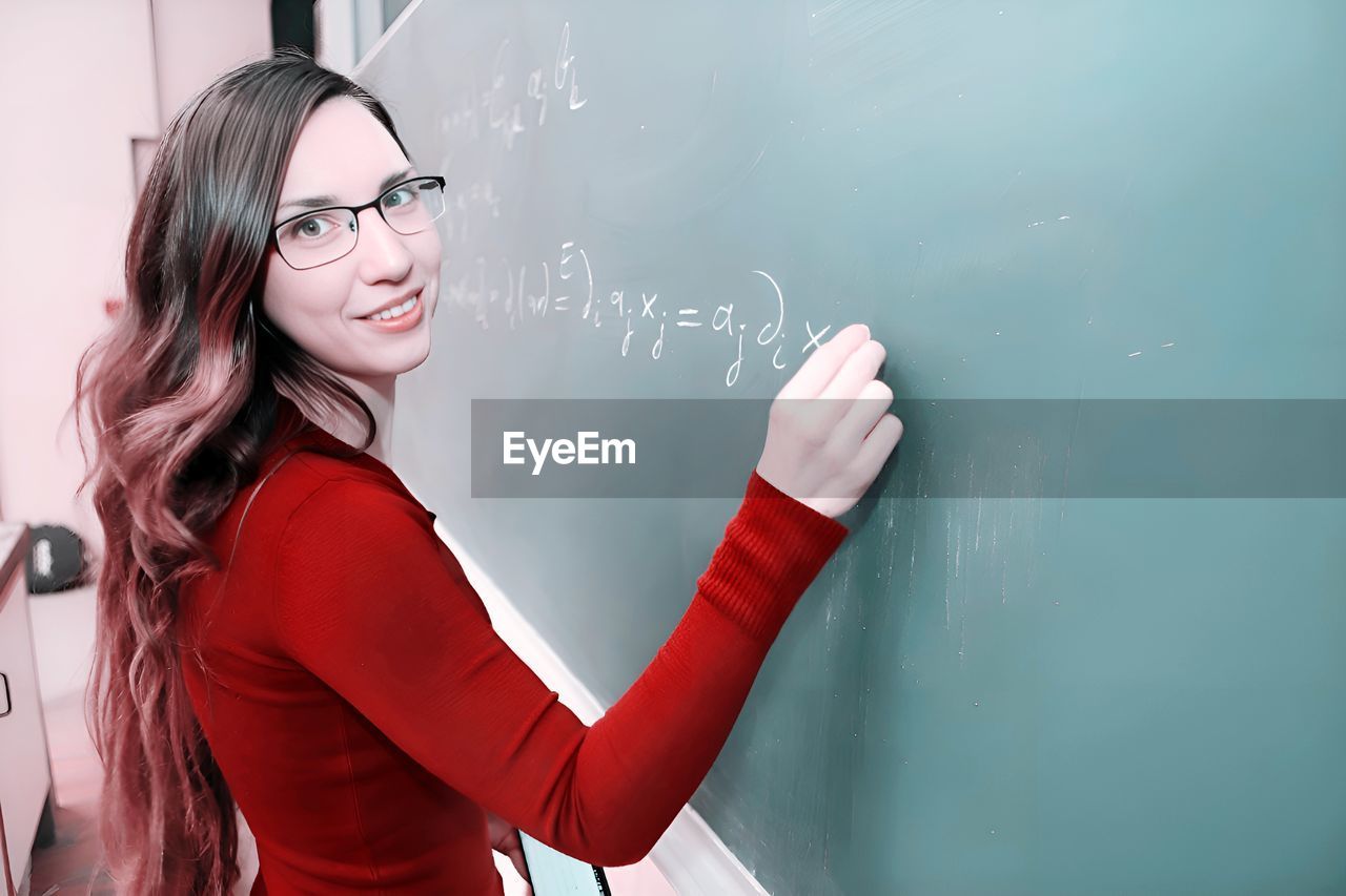 eyeglasses, board, women, glasses, education, one person, adult, blackboard, red, indoors, young adult, school, classroom, learning, smiling, waist up, long hair, emotion, happiness, portrait, standing, student, hairstyle, female, clothing, person, communication, casual clothing