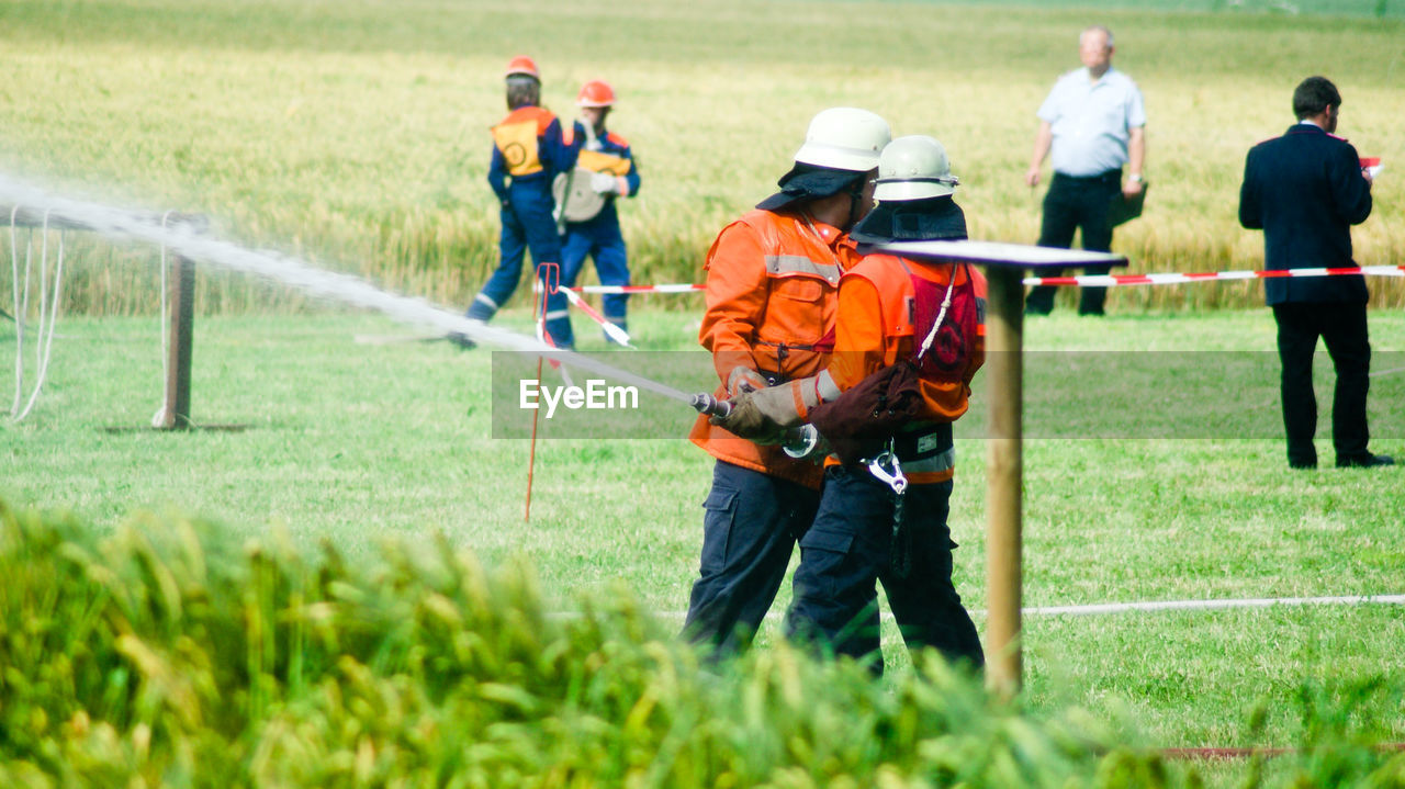 Firefighters spraying water from hose while standing on grass field