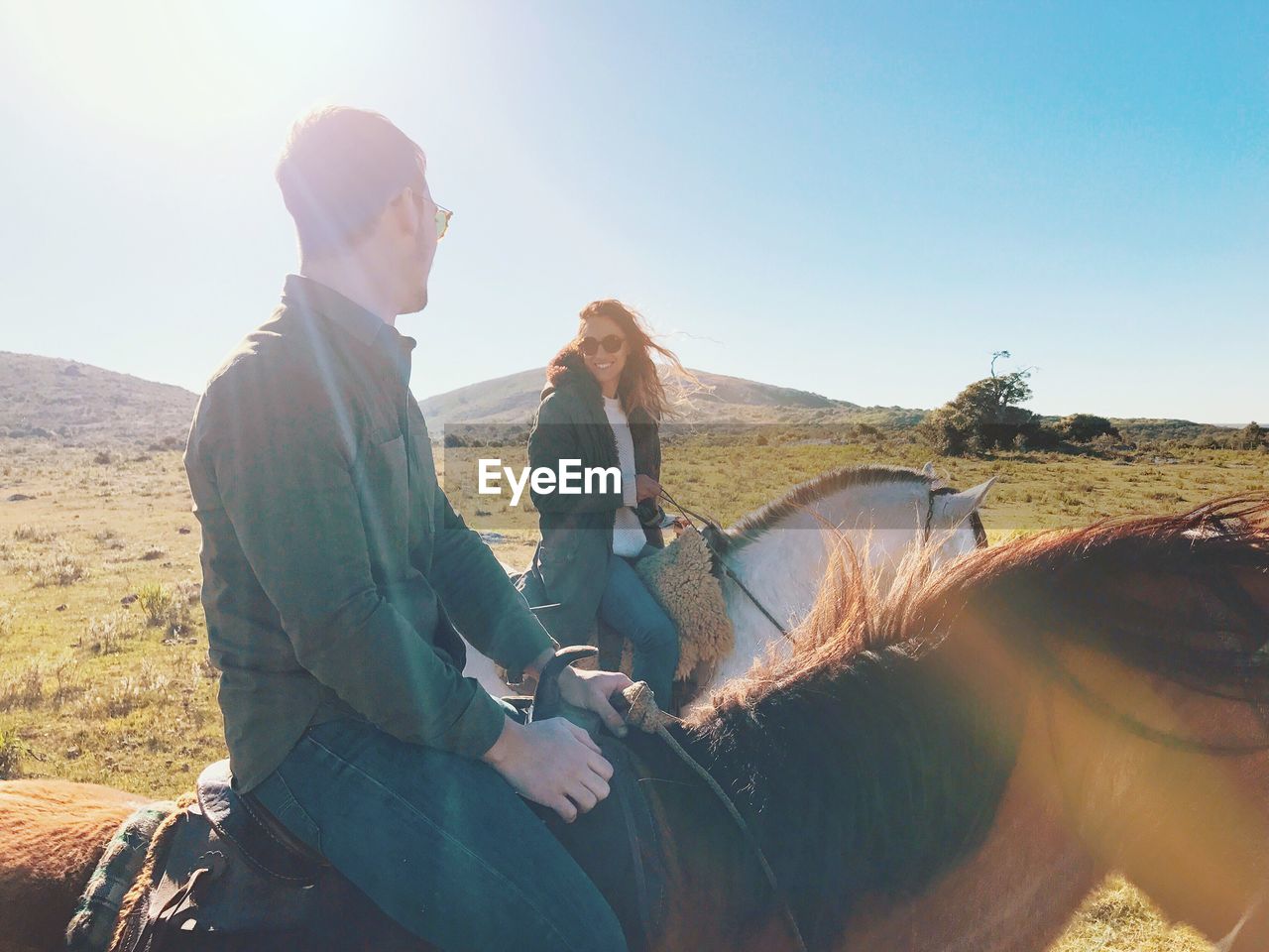Couple riding horses on land against clear sky during sunny day