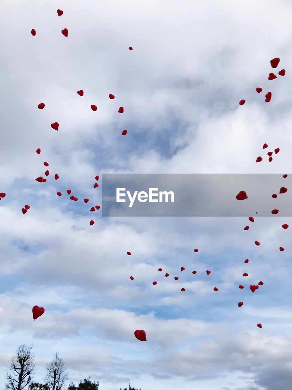 Low angle view of balloons flying against cloudy sky