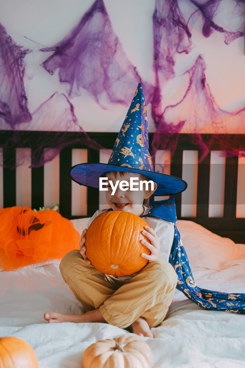 Little preschooler boy in festive halloween costume with a pumpkin lantern jack at home