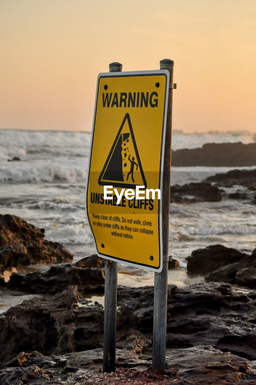 Warning sign on a beach with amazing sunset in the background with waves