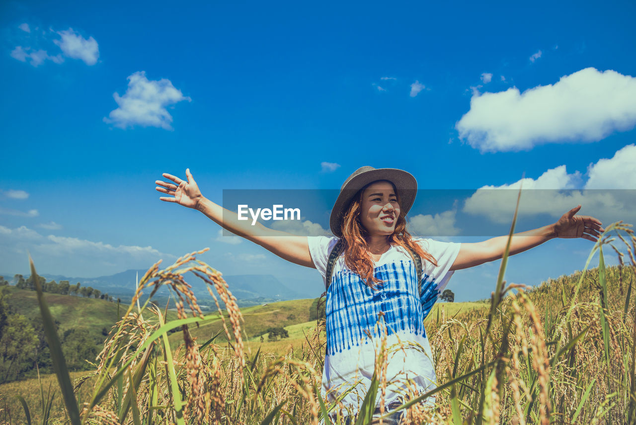 Smiling woman wearing hat standing on field against sky