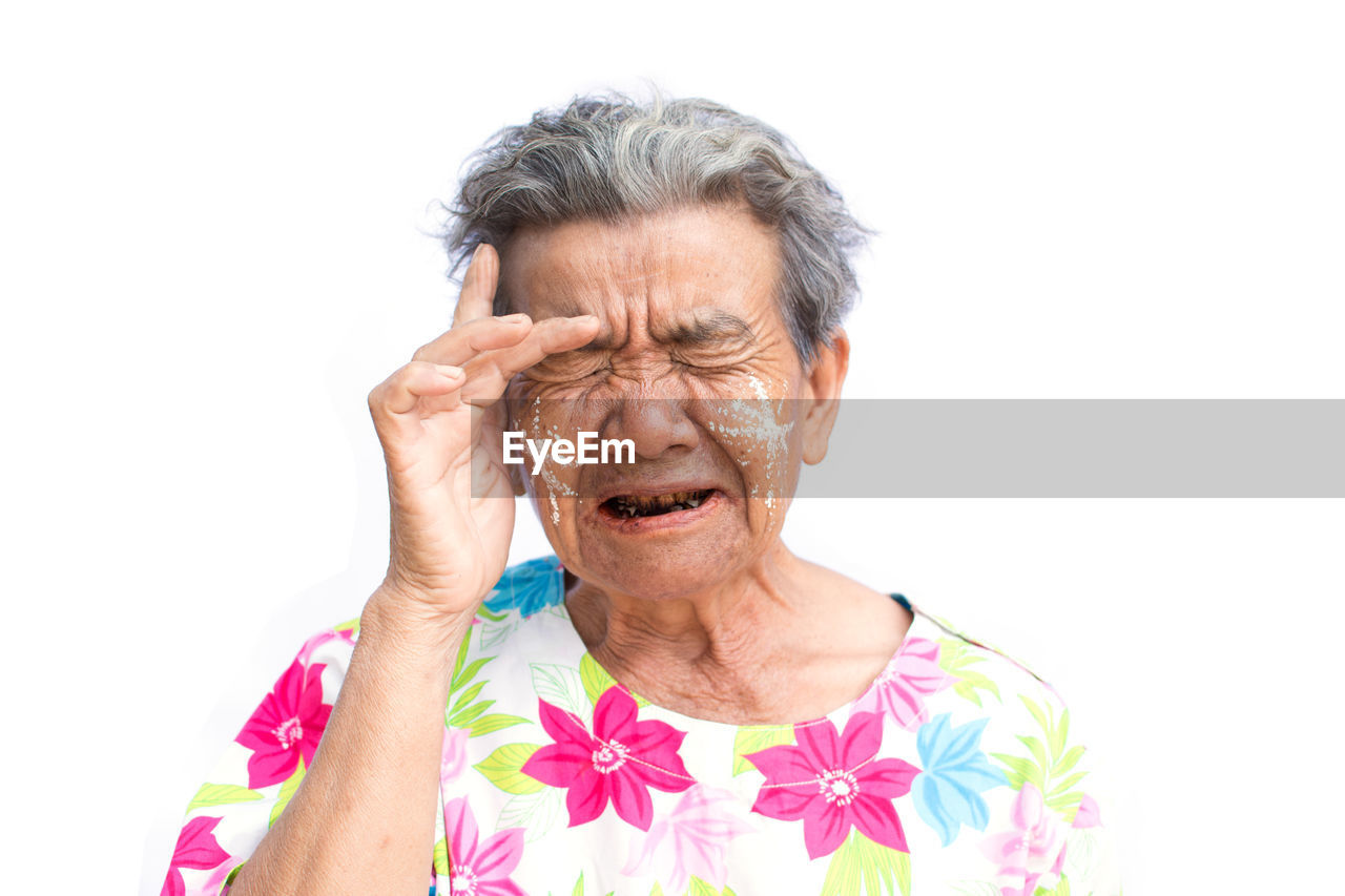 Close-up of tensed senior woman with eyes closed against white background