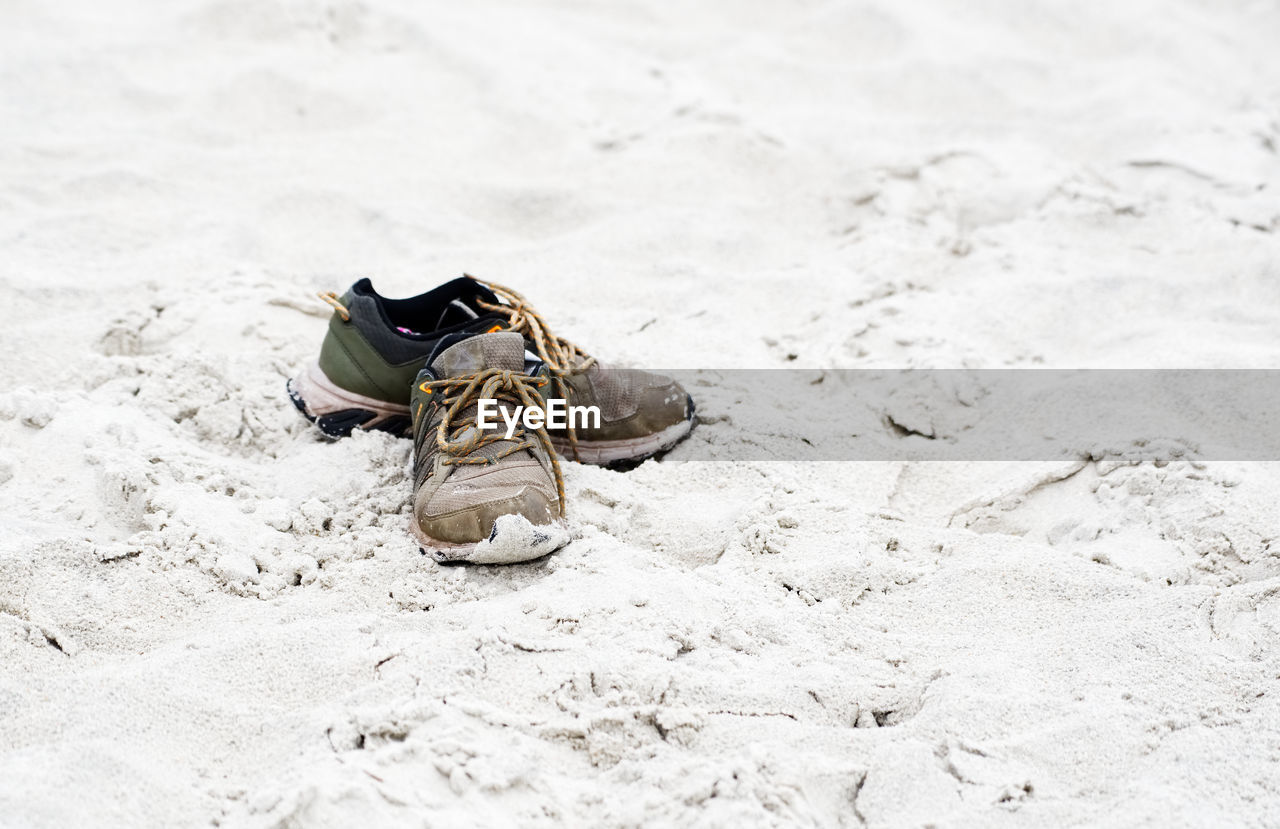 HIGH ANGLE VIEW OF SHOES ON SAND AT BEACH