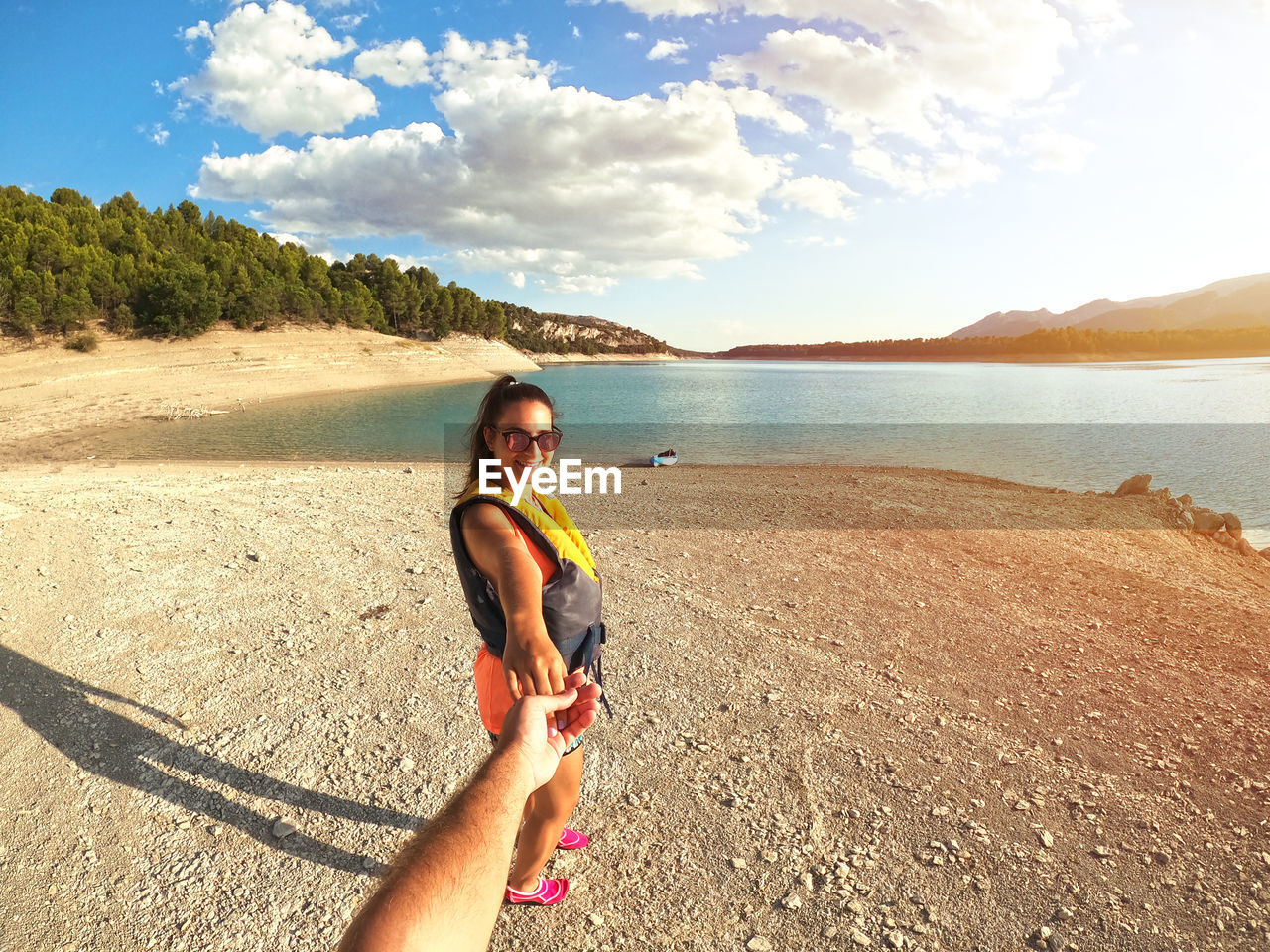 Portrait of smiling young woman holding hand on beach against sky