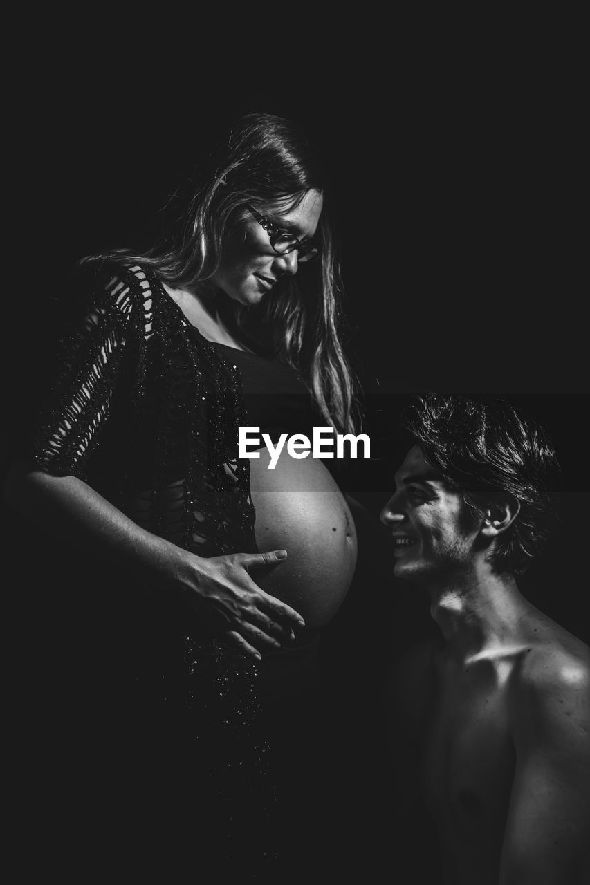 Man looking at pregnant woman belly against black background