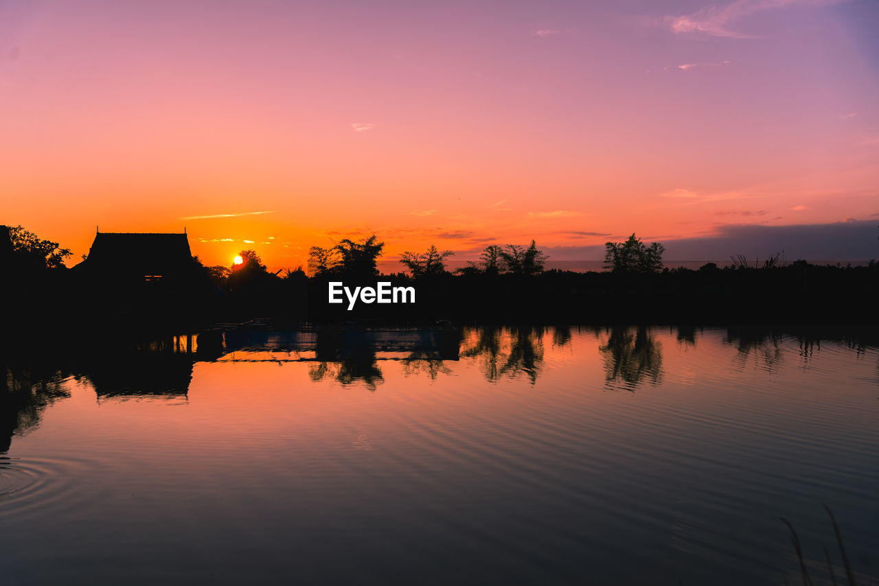 SILHOUETTE TREES BY LAKE AGAINST ORANGE SKY