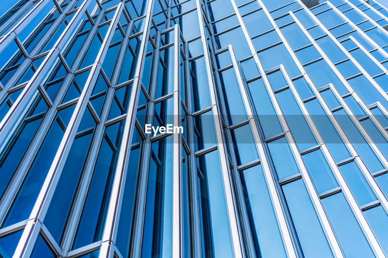 LOW ANGLE VIEW OF MODERN GLASS BUILDING AGAINST SKY